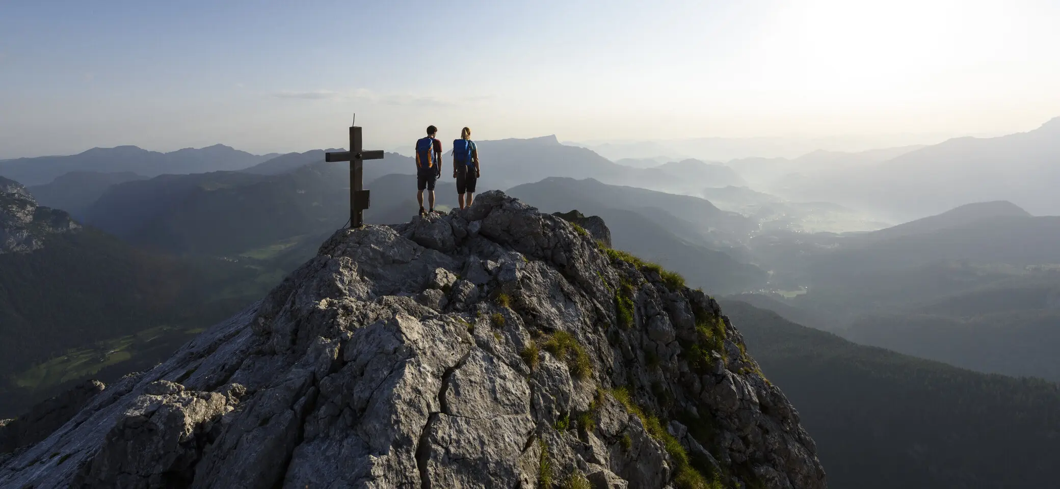 Zwei Wanderer auf einem Berggipfel mit Gipfelkreuz - aus der Ferne fotografiert | © DAV/Wolfgang Ehn